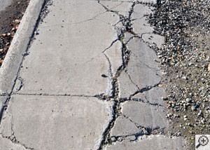 A severely damaged, sinking sidewalk with washed out sand underneath in Hurley.